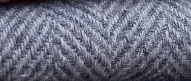 Close-up of a light grey herringbone wool: fine alternating diagonals, marled yarn.