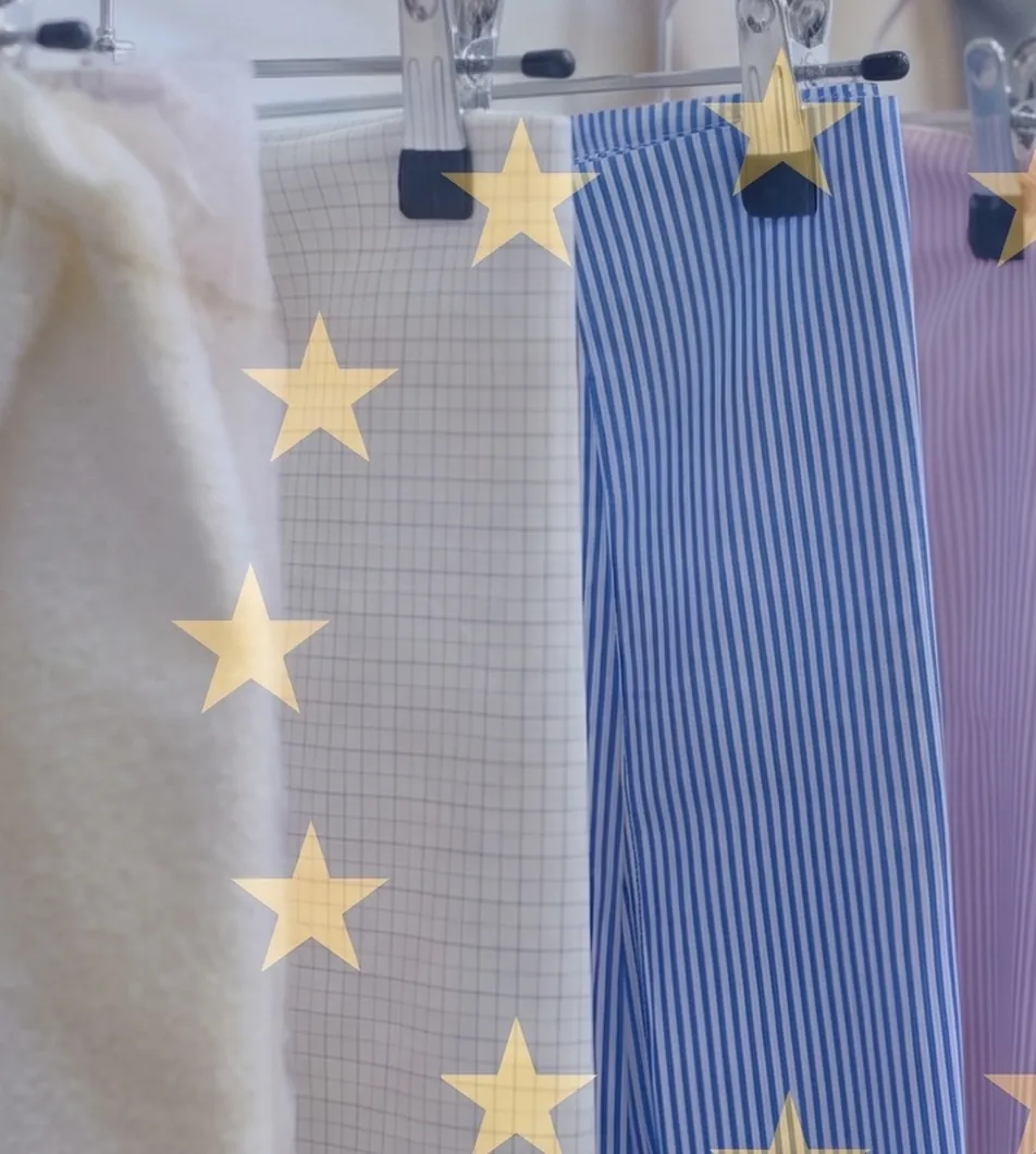 Light-coloured garments and fabric lengths hanging from the clips of a clothing rail, overlaid with large golden stars.